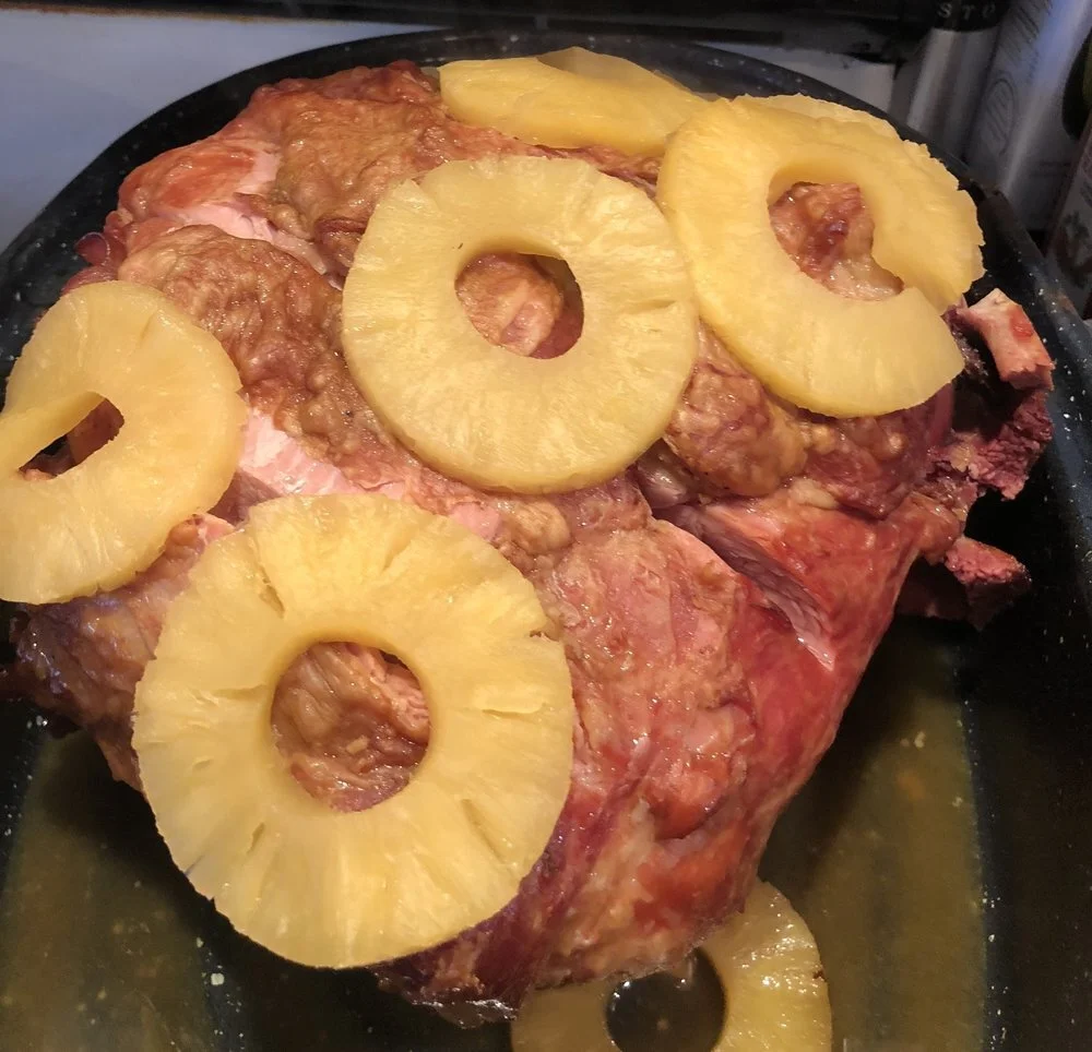Person holding a large piece of raw pork meat wrapped in butcher paper, showcasing the marbled texture and freshness of the cut against a dark kitchen backdrop.